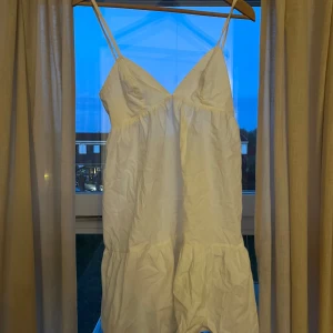 Vit kort klänning med volang och knytband - Säljer en söt vit kort klänning med smala axelband och volang nertill. Klänningen har v-ringning och öppen rygg med knytband. Det gör att den passar många! Använd ett fåtal gånger. Perfekt för sommarens varma dagar eller studentfirande. Pris kan alltid diskuteras💕