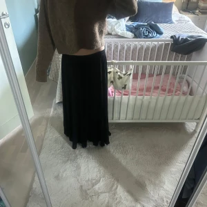 Svart långkjol - Säljer en svart långkjol med mjukt och flödande tyg. Kjolen har en enkel och stilren design utan synliga detaljer eller mönster. Perfekt för dig som gillar en klassisk och tidlös look.