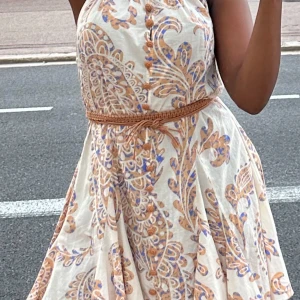 Beige midi klänning från Zara   - Säljer en beige midiklänning med blått och orange blommigt mönster. Klänningen har knappar framtill, ett flätat bälte i midjan och är ärmlös. Använt endast vid två tillfällen och är i princip ny i skicket. Inga defekter eller fel. Den har dragkedja på baksidan. 