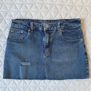 Blå jeanskjol med fickor - Säljer en klassisk blå jeanskjol med fem fickor och bälteshällor. Midjemåttet är ca 34cm och längden på kjolen är ca 29 perfekt längd enligt mig.   Kjolen är kort och har en liten sliten detalj framtill. Pris kan diskuteras 