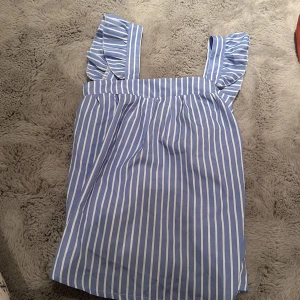 Blå- och vitrandig linne med volangdetaljer - Super söt till sommaren och fin knytning i ryggen. Super bra skick.