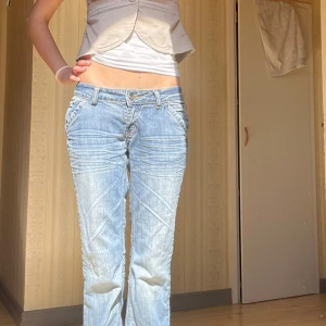 Lågmidjade ljusblå jeans - Assnygga blå lowwaist jeans med med snygga detaljer på fickorna. Säljer pga att dem blivit för korta för mig som är 177cm. Har några slitningar längst ner och ser smutsiga ut på bilden men tvättas självklart innan utskick.