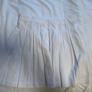 vit plisserad tenniskjol - vit tennisskjol köpt från new yorker! kjolen är veckad och stretchig i midjan. lätt missfärgad på baksidan (närbild på sista bilden) som går att bleka bort med fläckborttagning.