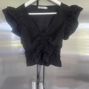 Svart blus med volang och knyt från Basic France - Säljer en svart blus från Basic France med volangdetaljer på axlarna och knyt framtill. Blusen har v-ringning med korta ärmar. Perfekt nu till sommaren. Det är storlek S/M men skulle säga att den mer är åt S hållet. Priset går att diskutera.