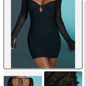 Svart kort klänning med pärlbroderade ärmar från OhPolly - Säljer en svart kort klänning med figurnära passform och långa, transparenta ärmar dekorerade med pärlor. Klänningen har en djup v-ringning med liten cut-out framtill och snörning i ryggen. Från OhPolly och använd 1 gång, storlek uk6