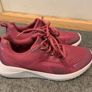 Rosa sneakers med vit sula - Säljer ett par snygga rosa sneakers med vit platt sula och snörning. Skorna har meshdetaljer för extra andningsförmåga och är perfekta för vardagsbruk eller lätt träning. Fräscha och trendiga skor som passar till många outfits. Aldrig kommit till användning 