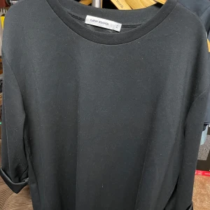 Carin Wester långärmad tröja stl L - En stilren svart långärmad tröja från Carin Wester i storlek L. Tröjan har en enkel och rak passform med rund halsringning och uppvikta ärmslut. Perfekt basplagg till garderoben.