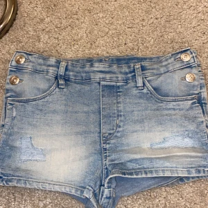 Ljusblå jeansshorts från &Denim - Ljusblå jeansshorts med slitningar och fyra silverfärgade knappar framtill. Klassisk femficksmodell och bälteshällor. Perfekta för varma dagar och har en snygg, något tvättad look.