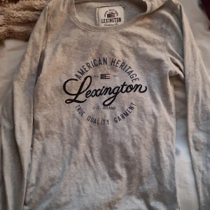 Grå långärmad tröja från Lexington - Säljer en grå långärmad tröja från Lexington med tryck på bröstet. Tröjan har rund halsringning och är tillverkad i mjuk bomull, perfekt för en avslappnad stil.