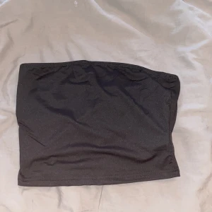 Svart tubtopp - Säljer en enkel svart tubtopp i stretchigt material. Perfekt att styla till olika outfits och passar bra till varma dagar. Sitter tight runt kroppen och är axelbandslös.