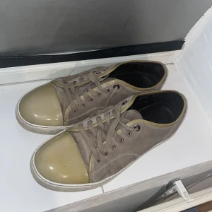 Grå/beige sneakers från Lanvin  - Säljer ett par grå sneakers från Lanvin med beige glans i storlek 43 (är dock som 44) har haft dom har i nårgra månader men inte kommit till användan. Obs snörrena är trasiga