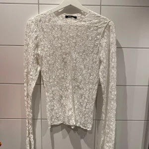 Vit spets topp från Gina Tricot - Säljer en vit långärmad topp från Gina Tricot i genombruten spets. Tight passform och rund halsringning. Perfekt att styla med jeans eller kjol för en trendig look.