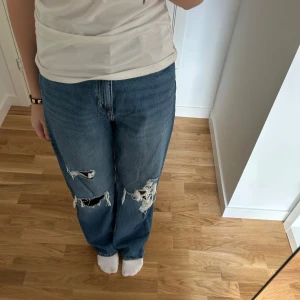 Blå wide jeans med slitningar från H&M - Säljer ett par blå jeans från H&M med bred passform i storlek 158, men passar också XXS. Jeansen har tydliga slitningar och hål på framsidan av benen. Klassisk femficksmodell och raka ben.