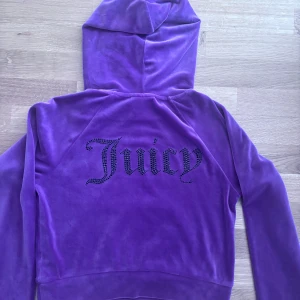Lila hoodie från Juicy Couture - Säljer en lila velour hoodie från Juicy Couture med huva och magficka. Baksidan har texten 'Juicy' i svarta stenar. 
