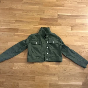 Olivgrön jeansjacka från Wow - Säljer en olivgrön jeansjacka från Wow i storlek 158. Jackan har klassisk krage, vita knappar framtill och två bröstfickor med lock. Perfekt för dig som gillar en enkel och stilren look. Är inte sådär grön i verkigheten, färgen syns mer på sista bilden. STORLEK 158!’