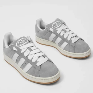 Grå Adidas Campus sneakers - Säljer ett par grå Adidas Campus sneakers med vita ränder och gummisula. Skorna har klassisk design med snörning och är tillverkade i mocka. Perfekta för dig som gillar stilrena och bekväma sneakers. Skickar med ett par extra nya tjocka campus skosnören, kan också byta till dem på skorna innan jag skickar om du som köper vill det💓💓