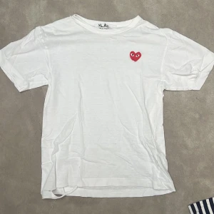 Vit t-shirt från Comme des Garçons Play - Galet fet tisha från CDG play!🔥Katastrofalt skick med flertal synliga hål därmed det OTROLIGT låga priset. Storlek S men passar mindre då den är väldigt liten i storleken, perfa för er lil jitz🔥Svarar alltid DM, pris såklart diskuterbart! Ny pris 1100kr från Paul and Friends på NK