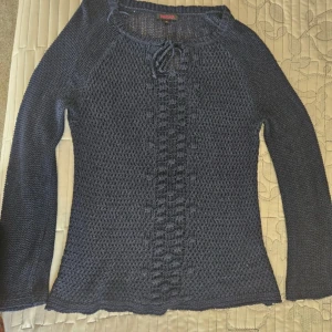 Mörkblå stickad tröja  - Säljer en mörkblå stickad tröja från Indiska med lång ärm och snygg knytning vid halsen. Tröjan har ett diskret mönster framtill och är perfekt för lager-på-lager-stil. Passar dig som gillar en klassisk och enkel look. 