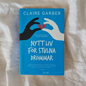 Nytt liv för stulna drömmar - En roman om att börja om efter ett brustet hjärta. Boken har blått omslag med illustration av två händer som håller i ett rött, trasigt hjärta. Perfekt för dig som gillar inspirerande och känslosamma berättelser.