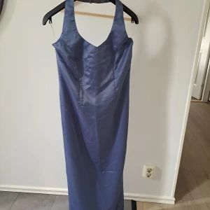 Lång blå satinklänning med breda axelband - Säljer en elegant långklänning i blå satin med breda axelband och urringning. Klänningen har en figurnära passform och är perfekt för bal eller festliga tillfällen. Ryggen är haltineck. Passar till längd ca 160.