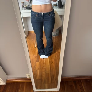 Mörkblå bootcut jeans från True Religion - Säljer ett par mörkblå jeans från True Religion med bootcut-passform och låg midja. Jeansen har klassiska kontrastsömmar, fem fickor och detaljerade bakfickor med knappar. Otroligt sparsamt använda! 