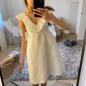 Vit volangklänning med v-ringning - Säljer en söt vit klänning med volangdetaljer och v-ringning. Klänningen är ärmlös och har en lätt strukturerad yta. Jättefin vit klänning från Bubbleroom. Aldrig använd och med lappen kvar. Perfekt till sommaren, student och skolavslutning! Kortärmad med fint mönster. Inte alls genomskinlig.