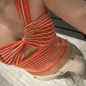 Röd- och vitrandig croppad topp med twistad detalj - Trendig croppad topp i rött med vita ränder och en unik twistad detalj framtill. Toppen har bred axelrem på ena sidan och är ärmlös, perfekt för sommarens alla tillfällen.