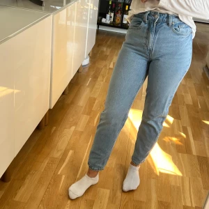 Ljusblå högmidjade jeans från H&M - Säljer ett par klassiska ljusblå jeans från H&M med hög midja och raka ben. Jeansen har fem fickor och stängs med dragkedja och knapp. Perfekta till vardags och lätta att matcha med olika toppar.