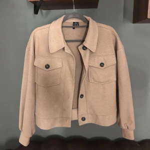 Beige jacka från Vero Moda - Snygg beige jacka från Vero Moda med klassisk krage och två stora bröstfickor med knappar. Jackan har lång ärm, knäppning framtill.