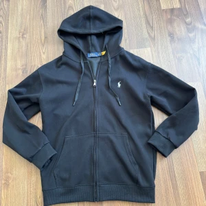 Svart hoodie från Polo Ralph Lauren - Svart hoodie från Polo Ralph Lauren med dragkedja framtill, huva med snörning och klassisk logga broderad på bröstet, säljes då den var lite för liten för mig. Passar M. Aldrig använd. 
