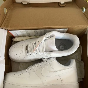 Nike Air Force 1 ’07 - Vita, Helt Oanvända, Storlek 41 (UK 7) - Säljer ett par helt oanvända Nike Air Force 1 ’07 i vitt. Skorna är i perfekt skick, aldrig använda, och kommer i originalförpackning. Storlek 41 (UK 7).