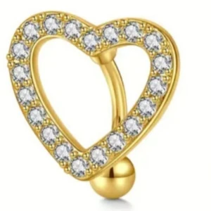 Guldfärgad hjärtformad navelpiercing - Superfin navelpiercing i guldfärg med hjärtform och glittrande stenar runt hela hjärtat. Perfekt accessoar för att ge din look extra bling och romantisk vibe.
