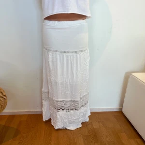 Vit långkjol med spetsdetaljer - Superfin vit långkjol med bred resår i midjan och snygga virkade spetsdetaljer. Modellen på bild är 171 cm lång.