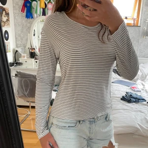 Randig långärmad tröja från Lindex - Säljer en vit långärmad tröja från Lindex med tunna svarta ränder. Tröjan har en avslappnad passform och är gjord i mjuk bomull, perfekt till jeans eller shorts. Enkel och stilren design som funkar året runt. Knappt använd. Säljer för jag inte använder den