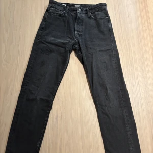 Svarta jeans Jack & Jones - Svarta jeans från Jack & Jones med diskreta slitningar på låret. Klassisk femficksmodell med dragkedja och knapp. Jeansen är tillverkade i mjukt denimtyg som sitter snyggt på benen. Modellen är Loose/Chris.