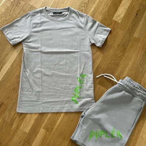Ljusgrå t-shirt och shorts från Duplér - Ljusgrå t-shirt och shorts från Duplér med korta ärmar och rund hals. Tryckt grönt Duplér-logo nertill på framsidan ger en cool touch. Perfekt för dig som gillar stilrena plagg med en twist. Skön och mjuk bomullskänsla.