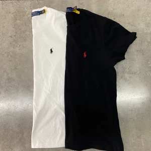 2-pack Polo Ralph Lauren t-shirts - Två klassiska t-shirts från Polo Ralph Lauren i bomull. En vit med mörkblå broderad logga på bröstet och en svart med röd broderad logga. Båda har rund hals och korta ärmar, perfekt basic till garderoben.