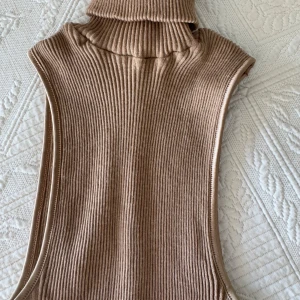 Beige ribbad stickad topp med polokrage från Intimissimi - Säljer en lång, ribbstickad väst i beige med hög polokrage. Linnet är ärmlöst och har en clean, minimalistisk look som är lätt att styla. 