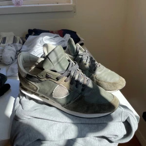 Gröna sneakers från Philippe Model - Snygga sneakers från Philippe Model i olika gröna nyanser med detaljer i mocka och textil. Skorna har vita och svarta detaljer på sulan, vit häl och svarta skosnören. Klassisk rund tå och platt sula för en stilren look.