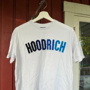 Vit HOODRICH t-shirt med blått tryck - Vit t-shirt från HOODRICH i bomull med stort broderat HOODRICH-tryck i olika blå nyanser över bröstet. Jag har använt den ett fåtal gångar och är lite uttvättat. Nypris går för 500kr. Storlek XS. 