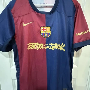 FC Barcelona Raphinha matchtröja Nike - Säljer en FC Barcelona matchtröja med Raphinha 11 på ryggen. Tröjan är kortärmad, i klassiska blå och vinröda färger med gul Nike-logga och klubbmärke på bröstet. Materialet är lätt och andas, perfekt för fotboll. Cactus Jack-tryck på framsidan och Champions League-märke på ärmen.