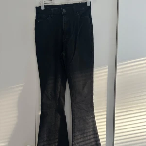 Svarta bootcut jeans med rå kant - Svarta jeans med bootcut-modell och rå, fransad midja. Klassisk femficksdesign och bälteshällor. Jeansen har en snygg utsvängd passform nertill och stängs med knapp och dragkedja. Perfekta för dig som gillar en trendig och avslappnad look. Byxorna är upp sydda. Folken finns kvar ifall att man vill göra dem längre