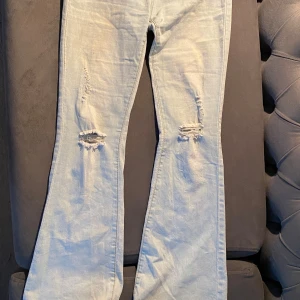 Ljusblå bootcut jeans med slitningar - Säljer ett par ljusblå jeans med bootcut passform och snygga slitningar vid knäna. Jag är 165 och passar nästan jättebra i längden!