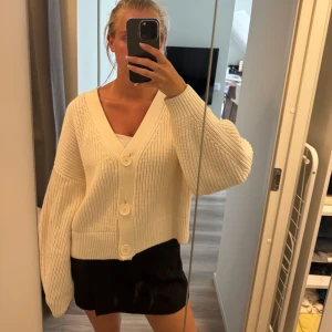 Vit oversized kofta med stora knappar - Supermysig vit kofta med oversized passform och stora dekorativa knappar framtill. Koftan är stickad i ett grovt mönster och har långa ärmar med breda muddar. Perfekt att slänga på sig över ett linne för en chill look.