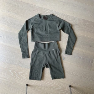 Träningsset Aimn - Snygg croppad långärmad träningströja från Aim'n i militärgrönt samt korta tights till. Tröjan har ribbade detaljer på ärmar och axlar, rund hals och är tillverkad i ett stretchigt material som andas. Perfekt för gymmet eller yoga.