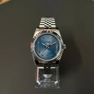 Seiko mod blue Arabic - Snygg Seiko automatisk klocka med blå urtavla och arabiska siffror. Boetten och länken är i silverfärgat rostfritt stål med en klassisk räfflad bezel. Länken är polerad och har en cool länkdesign som ger en modern vibe.