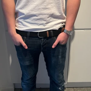 Svart flätat bälte med bruna skinn-detaljer från tressé - Snyggt svart flätat bälte från Tressé med bruna skinn-detaljer och silvrigt spänne. Perfekt accessoar för att lyfta din outfit med en stilren touch. Bältet har klassisk design och passar till många olika looks. Finns inte många kvar så skynda!!