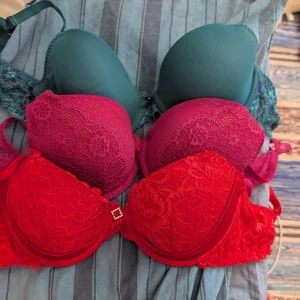 3 spets-bh:ar från Bodyflirt 80B - Säljer tre snygga bh:ar från Bodyflirt i storlek 80B. En är röd med spets och liten strassdetalj, en är mörkrosa med spets och en är mörkgrön med spetsdetaljer. Alla har vadderade kupor och fina spetsmönster. Perfekta för att ge lite extra färg i underklädeslådan.
