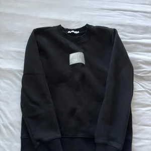 Svart sweatshirt från Calvin Klein Jeans - Svart sweatshirt från Calvin Klein Jeans med en silverfärgad CK-logga på bröstet. Tröjan har rund halsringning, långa ärmar och ribbade muddar. Perfekt för en clean och stilren look.