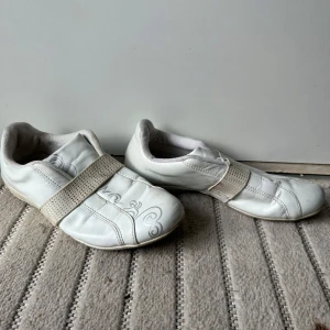 Vita sneakers med broderidetalj - Snygga vita sneakers från Z-O med coolt broderat mönster på sidan och bred resår över foten. Skorna har rund tå, platt sula och är gjorda i syntetmaterial. Perfekta för dig som gillar stilrena och sportiga skor med en twist.